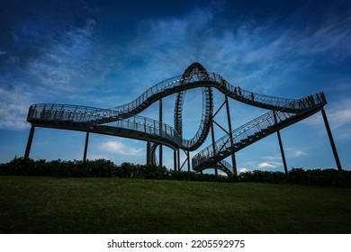 Tiger And Turtle, A Walkable Roller Coaster Sculpture On Magic Mountain Against A Dark Cloudy Sky At The Blue Hour, Art Installation And Landmark In Angerpark Duisburg, Germany, Copy Space