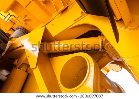 Tight angled close-up showing interconnected yellow-painted metal parts of heavy industrial machinery, including circular openings, cylindrical shafts, bolted