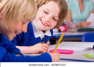 A Tight Closeup Of Two Cute Smiling Children In A Classroom Under Selective Focus Wearing School Uniform Solving Their Math Problems Having Their Teacher Sitting In The Background