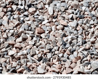 Tight overhead view of a dense layer of small mixed gravel stones in pale gray, beige, white, and pink tones scattered across the ground. Irregular angular