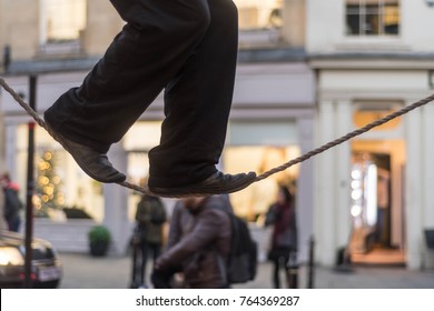 Tight Rope Walker's Legs. Feet Of Acrobat Balancing On Rope In Busy High Street With Passers By