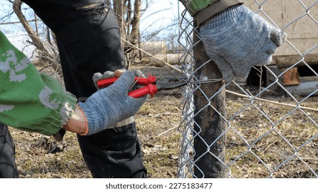 tightening the wire with pliers on a galvanized mesh fence in the process of fencing a suburban area, building a metal mesh fence in a country house locally using wire cutters