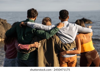 A tight-knit group of friends stands together, gazing out at the sea, sharing a tranquil moment by the ocean, signifying unity and contemplative peace - back view. - Powered by Shutterstock