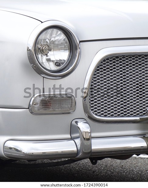 Tightly framed\
photo of retro white car with round headlight, billet grille, and\
shiny chrome bumper and\
trim.