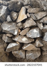 A tightly packed yet irregular stack of rough-textured natural stones, colored in a blend of gray and brown. Some stones bear patches of moss and white marks, creating a natural appearance with remnants of dried leaves tucked into the crevices.