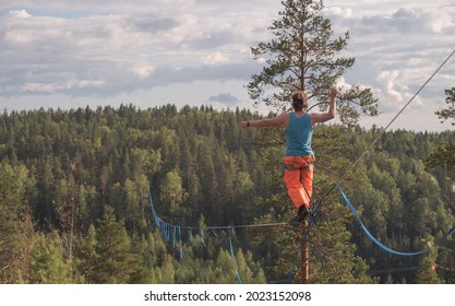 A tightrope walker walks along a long highline above the forest. Back view - Powered by Shutterstock