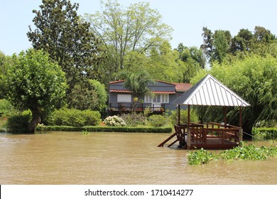 Tigre Delta In Argentina, River System Of The Parana Delta North From Capital Buenos Aires. Lush Vegetation, Traditional Wood House By Wooden Pier And Orange Water That Carry Clay To Rio De La Plata.