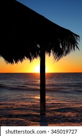 Tiki Hut On Beach At The Sunset With Surfer In Ocean