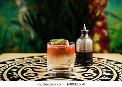 A Tiki Style Colourful Layered Cocktail In A Rocks Glass With Crystal Clear Ice Cube, Garnished With A Mint Leaf