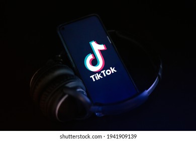 TikTok Logo On The Screen. Smartphone And Modern Headphones On Black Background Illuminated With Dark Blue Spotlight. Horizontal Shot. Rome, Italy- 3.23.2021 