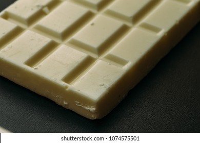 Tile or bar of white chocolate on black background, macro photo, selective focus