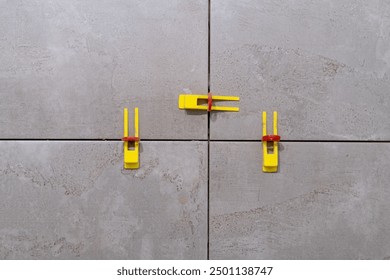 Tile leveling system with plastic clips and wedges in action. Ensures precise tile alignment. Perfect for showcasing tiling techniques and construction tools.