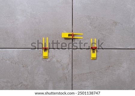 Tile leveling system with plastic clips and wedges in action. Ensures precise tile alignment. Perfect for showcasing tiling techniques and construction tools.
