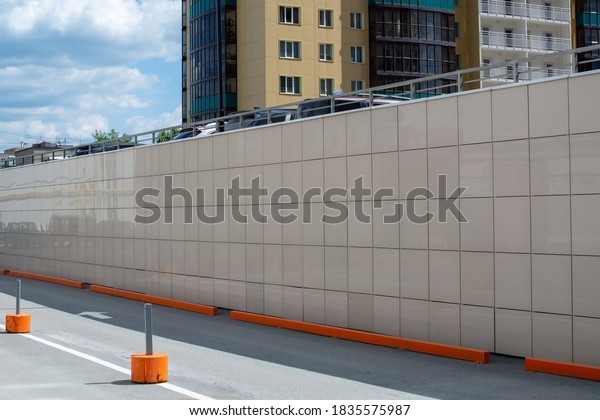 Tiled wall in the parking lot of a multi-level
business center. Equipped urabistic multilevel parking with fences
and signs. Silhouettes of parked cars. Light brown background with
sky and copy space.