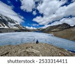 Tilicho Lake - May 25, 2024 - Lone trekker sitting next to Nepal flag overlooking half frozen Tilicho Lake.