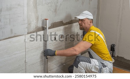 Tiling with large format tiles. A tiler measuring the verticality of the tile by a spirit level.