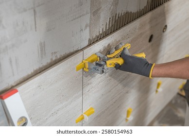 Tiling with large format tiles. The tiler's hands leveling tiles using pliers for levelys system.