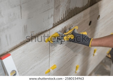 Tiling with large format tiles. The tiler's hands leveling tiles using pliers for levelys system.