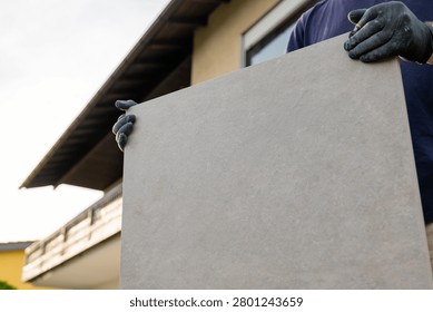  tiling work. Man carrying large paving tile for patio installation near house. Construction worker transporting a large tile slab for terrace . professional tiling work.