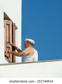 TILOS, GREECE-AUG 23: Typical Greek Man Working On Day Time On Aug 23, 2014.Daily Life Of Greek People In Small Village Of Tilos Island, Greece. Old Man Painting House, Life Style In Greece