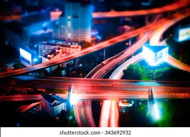 Tilt shift blur effect. Abstract cityscape background. Futuristic night aerial view of highway interchange with moving cars. Bangkok, Thailand