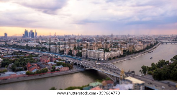 Tilt and\
shift view of sunset panorama of Moscow with pink clouds, bridge,\
traveling boats and river\
reflections