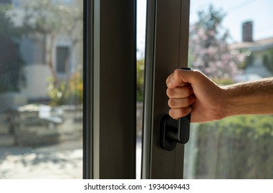 Tilt and turn grey color aluminum window, man holding the handle, fresh air for home. Male hand vertical open metal or PVC window, closeup view.