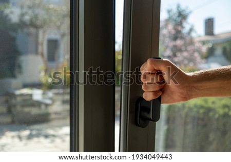 Tilt and turn grey color aluminum window, man holding the handle, fresh air for home. Male hand vertical open metal or PVC window, closeup view.