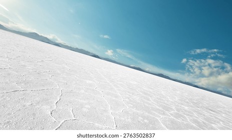 Tilted perspective of an empty white salt flat desert under a bright blue sky. Abstract cracked earth texture background with mountains on the horizon. Wide panoramic landscape for automotive or product placement.