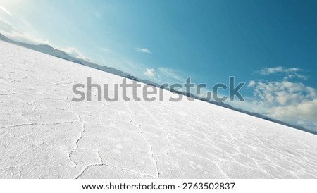Tilted perspective of an empty white salt flat desert under a bright blue sky. Abstract cracked earth texture background with mountains on the horizon. Wide panoramic landscape for automotive or product placement.