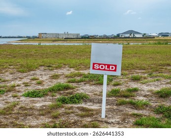 Un letrero de bienes raíces inclinado, “Vendido”, publicado en un lote baldío a cierta distancia de casas nuevas construidas o en construcción por un lago artificial en un desarrollo residencial suburbano en el suroeste de Florida