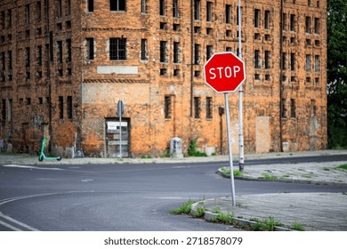 A tilted red STOP sign at an intersection against the backdrop of an old windowless building. The STOP sign has a blurred background.