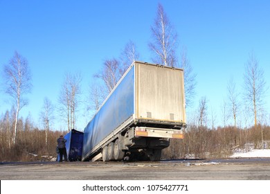 Tilted semi truck in roadside ditch – vehicle crash, skid, black ice, road accident on day winter road on trees and blue clear sky background. Sad driver call on the phone.