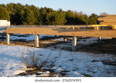 Timber frame base on piles, early construction stage, structural setup, wood beams, frame mounting process, carpentry, foundation wood, outdoor worksite.