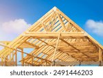 Timber framing stage of a new residential home attic construction using trusses for roof structure. A construction site set against a clear blue sky.