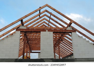 A timber roof truss in a house under construction, walls made of autoclaved aerated concrete blocks, a rough window opening, a reinforced brick lintel, blue sky in the background