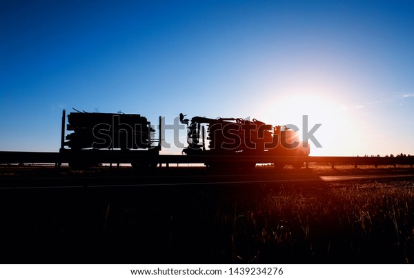 Timber truck transports timber logs and timber\
against the backdrop of a sunset and a blue sky, logistics and\
freight concept, copy\
space