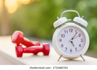 Time 5 Oclock Morning For Exercising Alarm Clock And Dumbbells On Green Natural Background Outside, Sport And Workout Concept