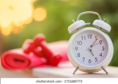 Time 5 Oclock Morning For Exercising Alarm Clock,blurred Dumbbells And Yoga Mat On Green Natural Background Outside With Sunlight, Sport And Workout Concept