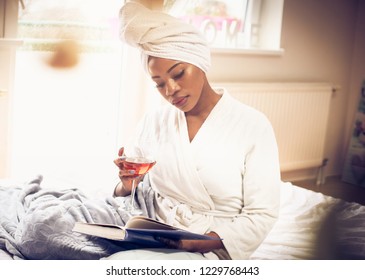 Time For Book And Glass Of Wine. African American Woman On Bed Reading Book And Holding Glass With Wine. Space For Copy. Close Up.