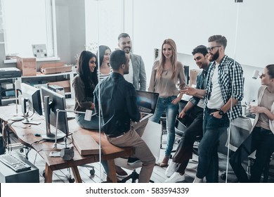 Time for brainstorming.  Full length top view of young modern people in smart casual wear talking and smiling while standing behind the glass wall in creative office