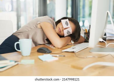 Time for a catnap. Shot of a tired businesswoman napping at her desk with adhesive notes on her eyes.