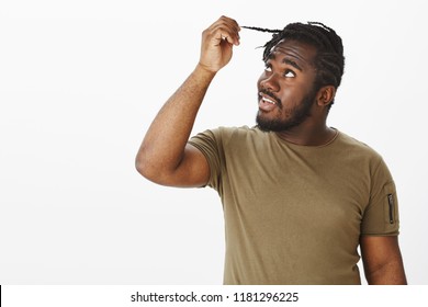 Time To Change Hairstyle. Good-looking African Guy With Beard In Military Outfit, Touching Hair Strand And Gazing At It With Curiousity, Wanting Cut Hair And Standing Against Gray Background