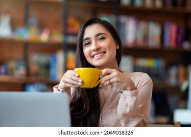 Time For Coffee. Pretty Latin Woman Sitting At Cafe Alone, Enjoying Cup Of Coffee And Smiling To Camera, Resting From Work, Having Break In Cafeteria