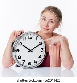 Time Concept - Smiling Beautiful Young Blond Woman Pointing To A Clock, Showing Patience And Relaxed Management Of Deadlines, White Background