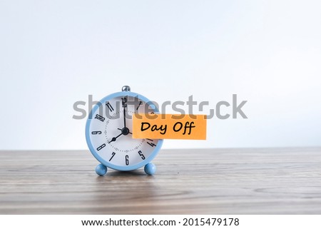 Time for day off concept with a message on Day Off written on the paper sticker and stick to the alarm clock.  Noise is visible due to the texture of the subjects