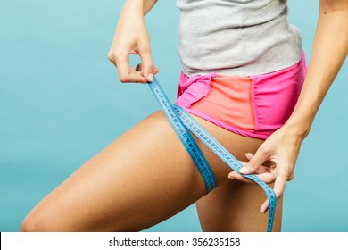 Time For Diet Slimming Weight Loss. Fitness Woman Fit Girl In Sportswear With Measure Tape Measuring Her Thigh On Blue