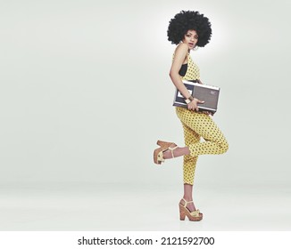 Time to disco. A young woman wearing a 70s retro jumpsuit holding a cassette player and striking a disco pose. - Shutterstock ID 2121592700