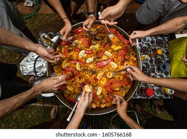 It's time to eat a paella. Several hands with cutlery begin to eat homemade paella in pure Spanish style. A sea and land paella.