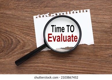 Time To Evaluate. text on magnifier glass on wood background